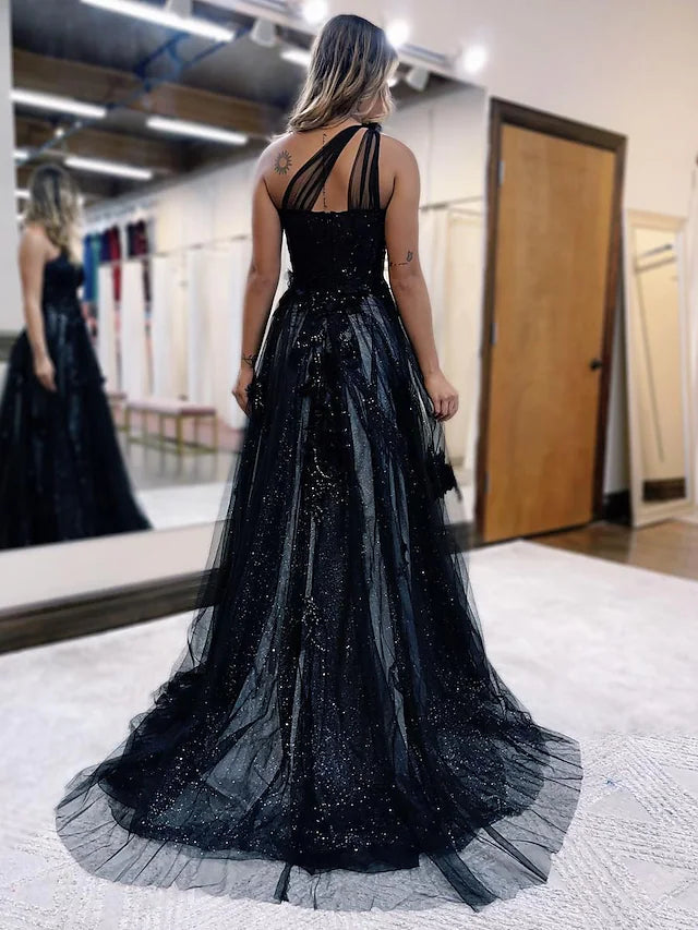 Close-up of the back of a one-shoulder tulle prom dress, showing backless detail and appliques.