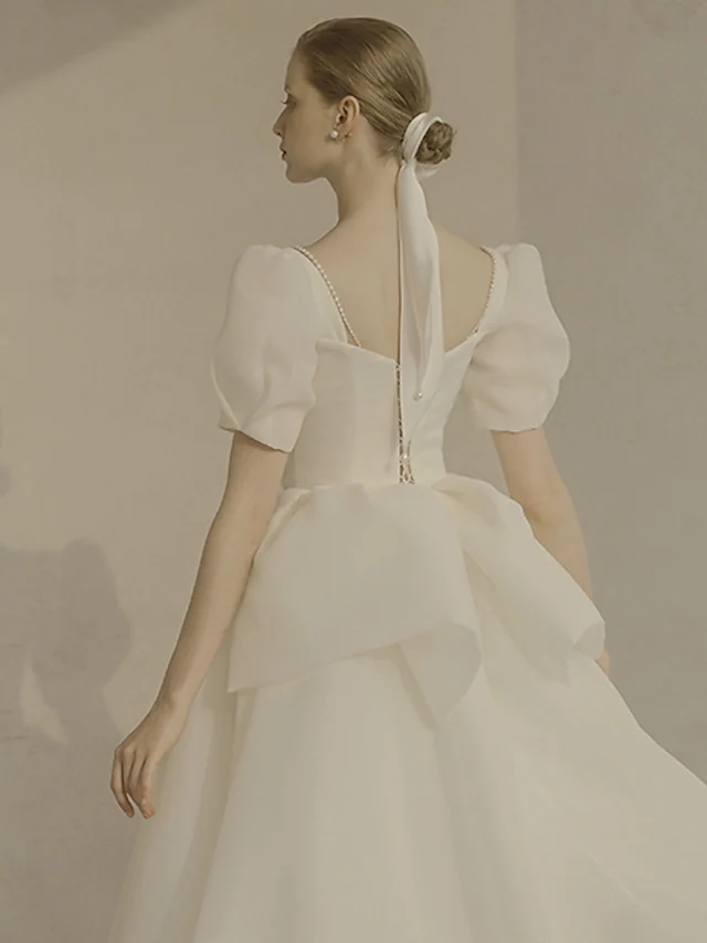 Side view of an A-Line scoop neck short sleeve white organza wedding dress with ruffles.