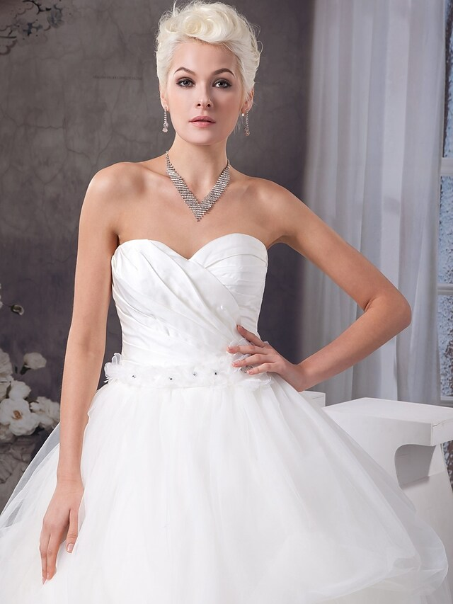Close-up of ruched and beaded details on a white wedding dress.