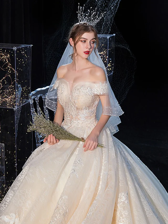 Full length view of a bride wearing an off-shoulder ball gown wedding dress.