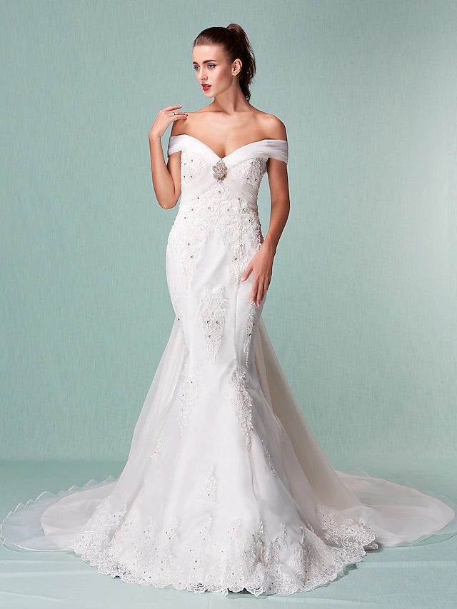 Close-up of beading appliques and crystal floral pin on an off-shoulder wedding dress.