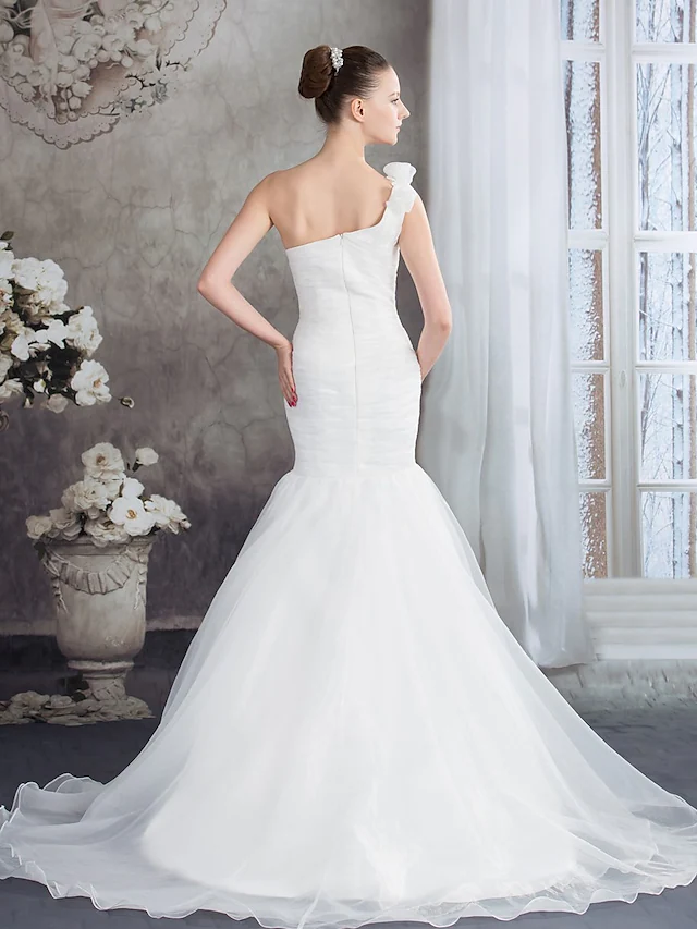 Full length view of a bride wearing an organza one-shoulder wedding dress.