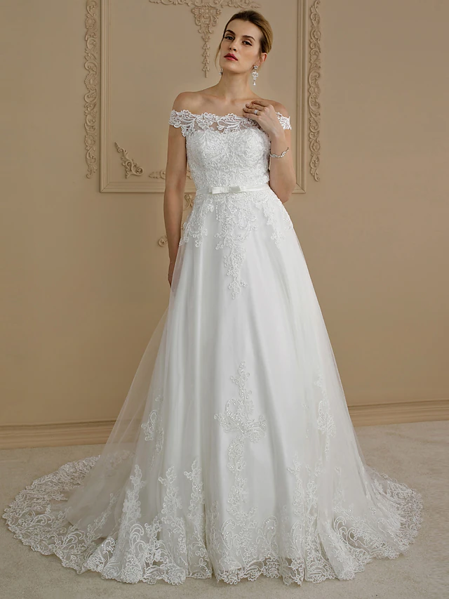 Side view of a bride wearing a glamorous off-shoulder wedding dress with a flowing court train.