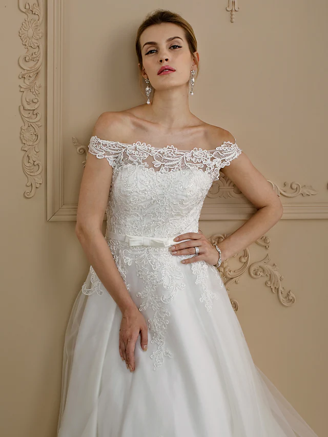 Close-up of the delicate lace and tulle fabric on an off-shoulder wedding dress.