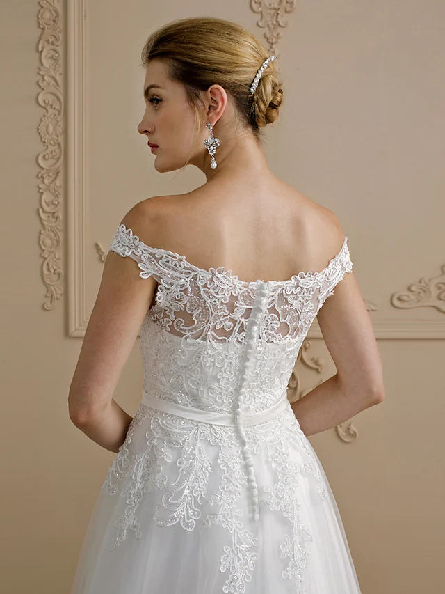 Bride posing in a backless off-shoulder ball gown wedding dress with sashes and ribbons.