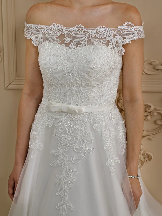 Full length view of a plus size off-shoulder wedding dress with cap sleeves and a voluminous skirt.