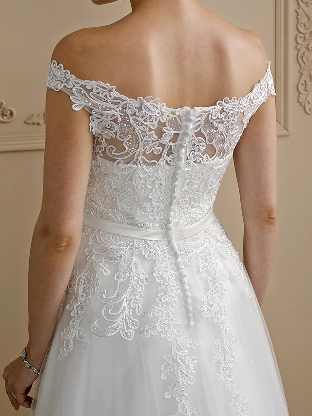Detailed view of the off-shoulder neckline and cap sleeves of a lace tulle wedding gown.