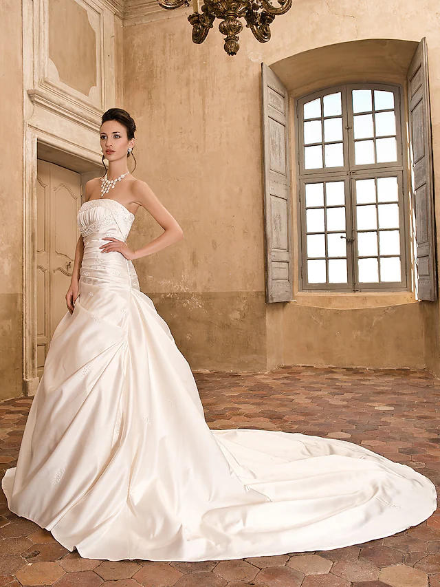 Side view of a bride wearing a strapless A-line satin wedding gown.