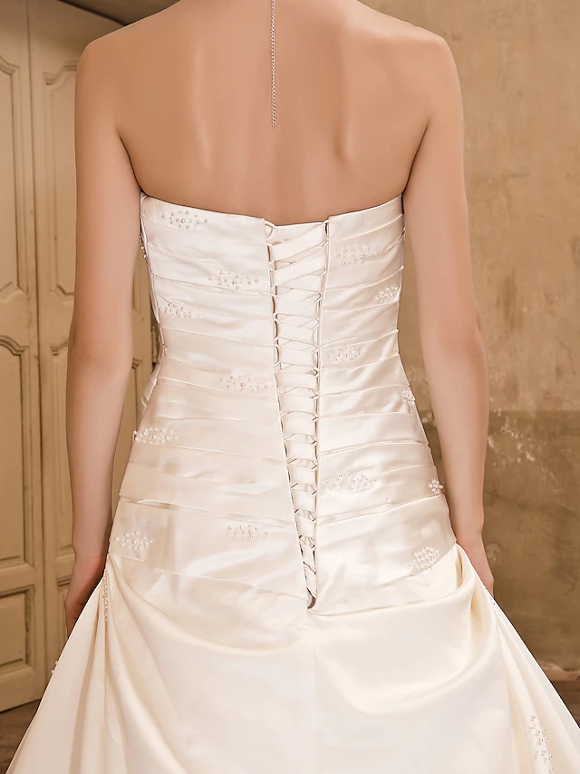 Full length view of a strapless satin wedding dress with a flowing chapel train.