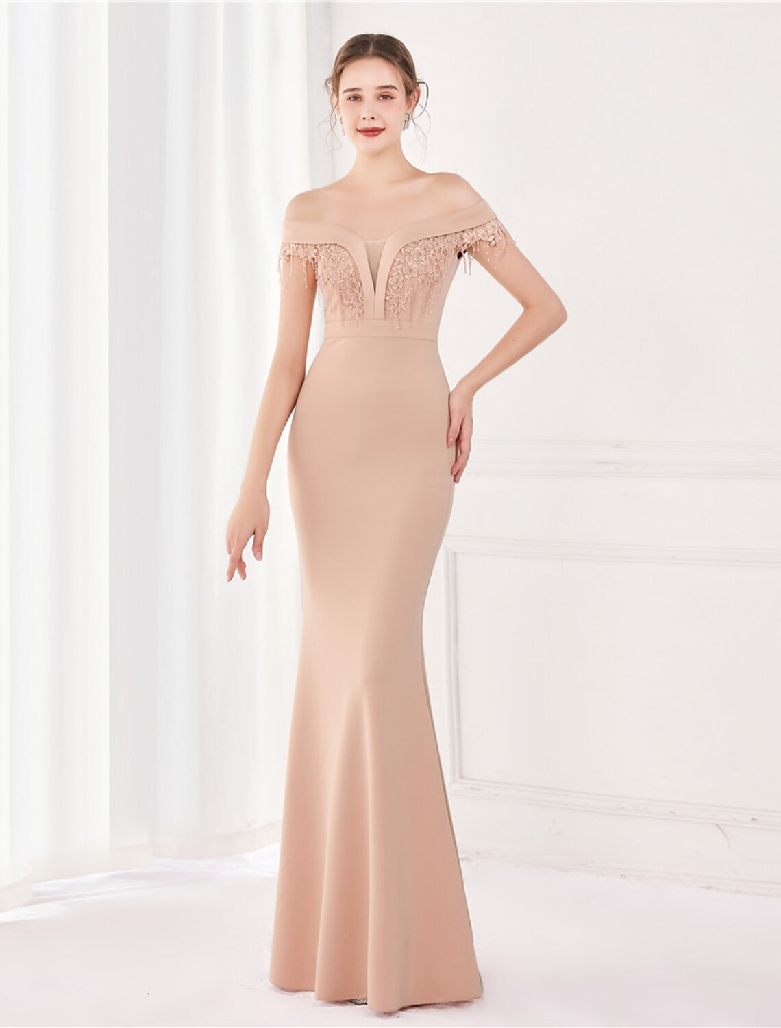 A woman wearing an elegant off-shoulder satin mermaid trumpet gown with short sleeves and a floor-length skirt.
