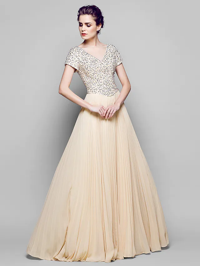 A woman models an elegant sparkling A-line mother of the bride gown with a bateau neck and short sleeves.