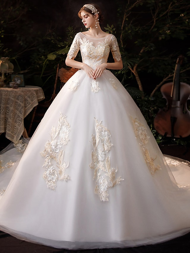 Bride in a white princess ball gown wedding dress with a jewel neck and short lace sleeves.