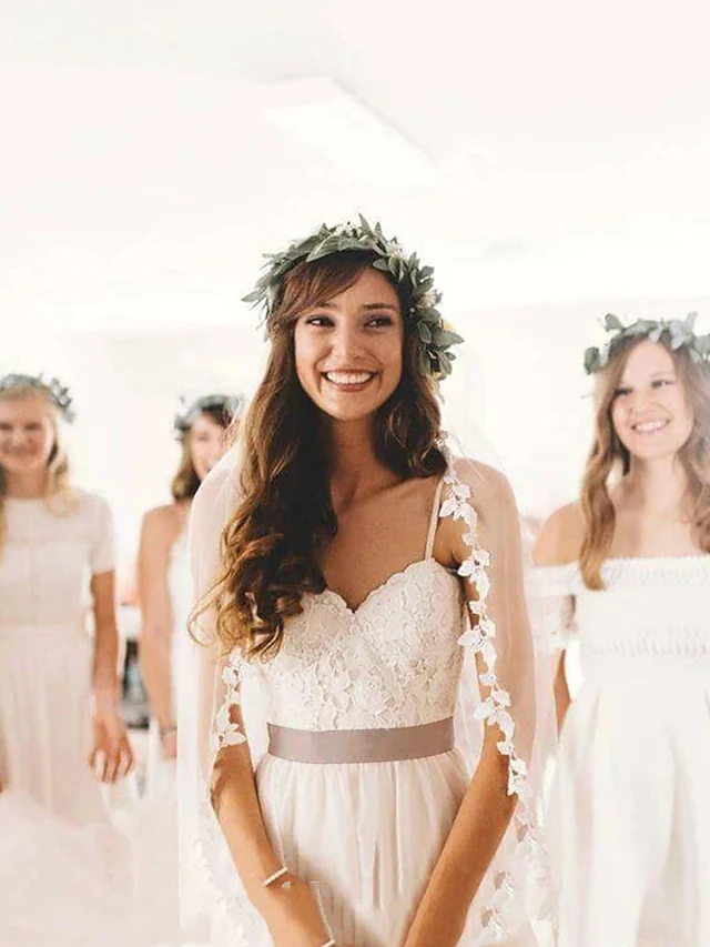 Side view of a bride wearing a white lace and tulle wedding dress with spaghetti straps and a flowing court train.
