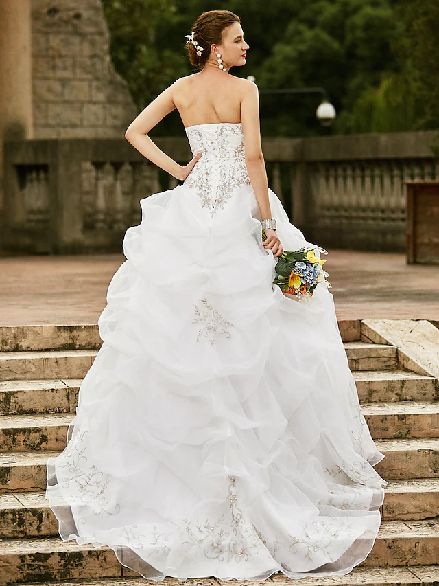Side profile of a bride wearing a strapless ball gown wedding dress with a pick-up skirt detail.