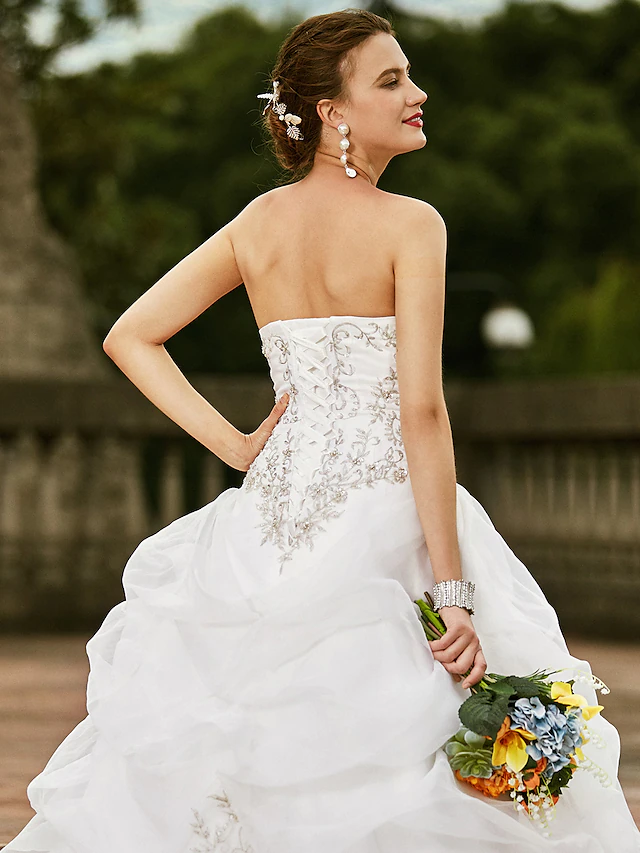 Full length view of a bride posing in a strapless embroidered ball gown wedding dress.