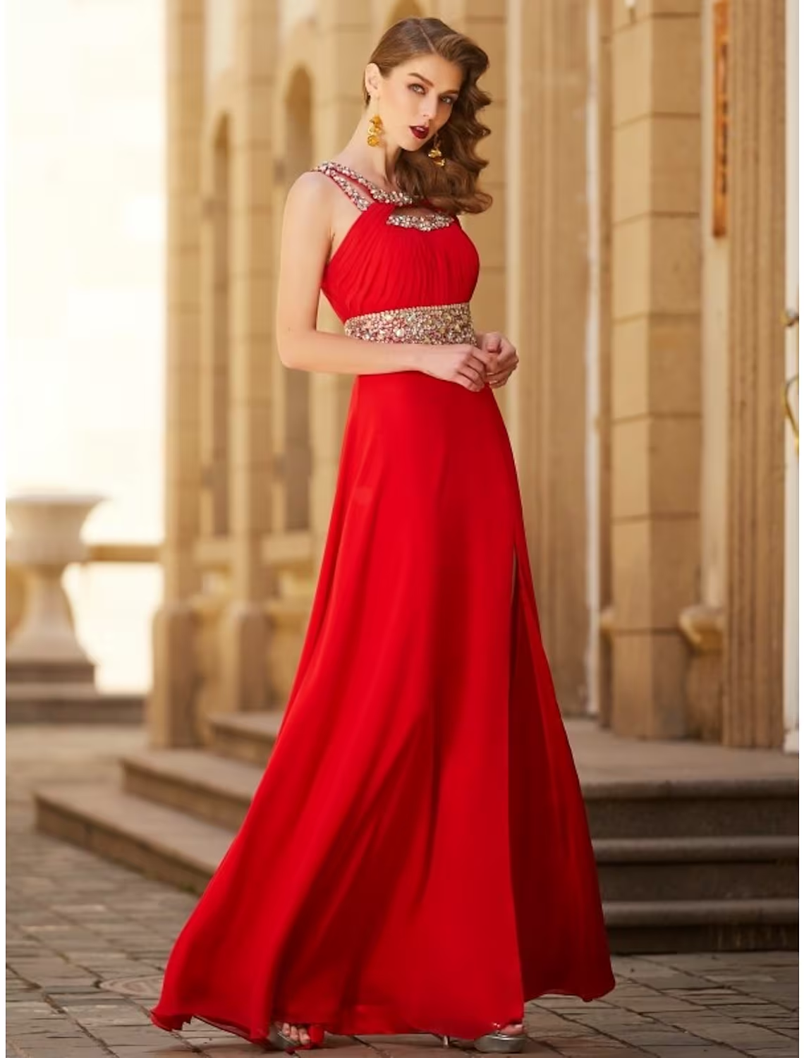 Woman posing in a sparkling A-line halter evening gown with a rhinestone slit.