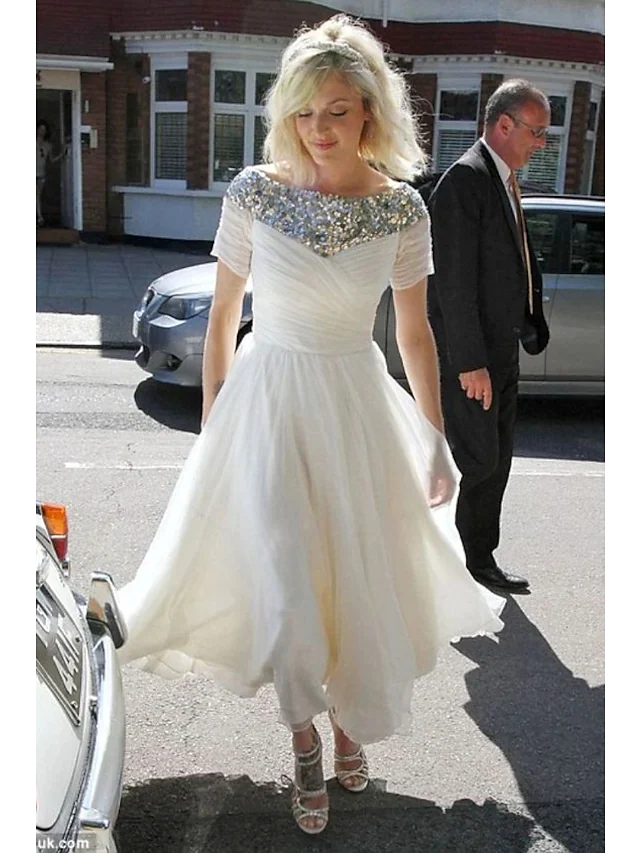 Model wearing a sparkling A-Line jewel neck tea length wedding dress with short sleeves and sequin details.