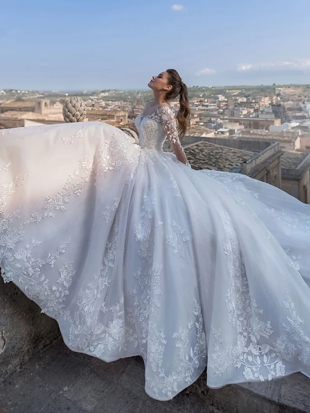 Full view of the sparkling V-neck ball gown wedding dress with long illusion sleeves and chapel train.