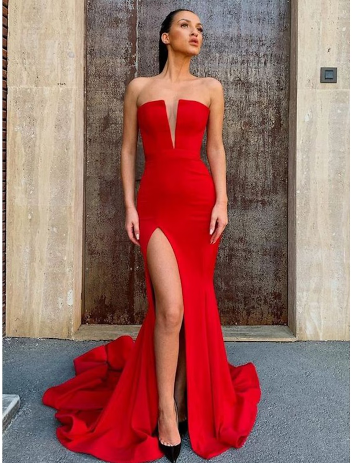 Back view of a woman wearing a strapless mermaid trumpet prom dress, highlighting the open back and flowing court train.